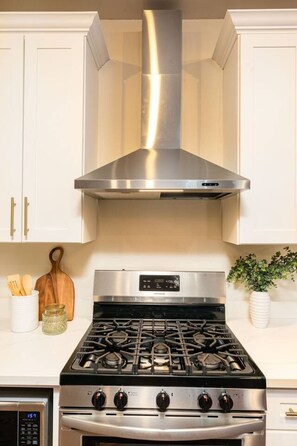 A kitchen with a stainless steel range hood, a stove with four burners, and white cabinetry. - Walk to Bourbon | Spacious & Bright 2BD in CBD (New Orleans)