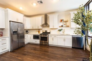 A modern kitchen with white cabinets, stainless steel appliances, and a wooden floor. - Walk to Bourbon | Spacious & Bright 2BD in CBD (New Orleans)