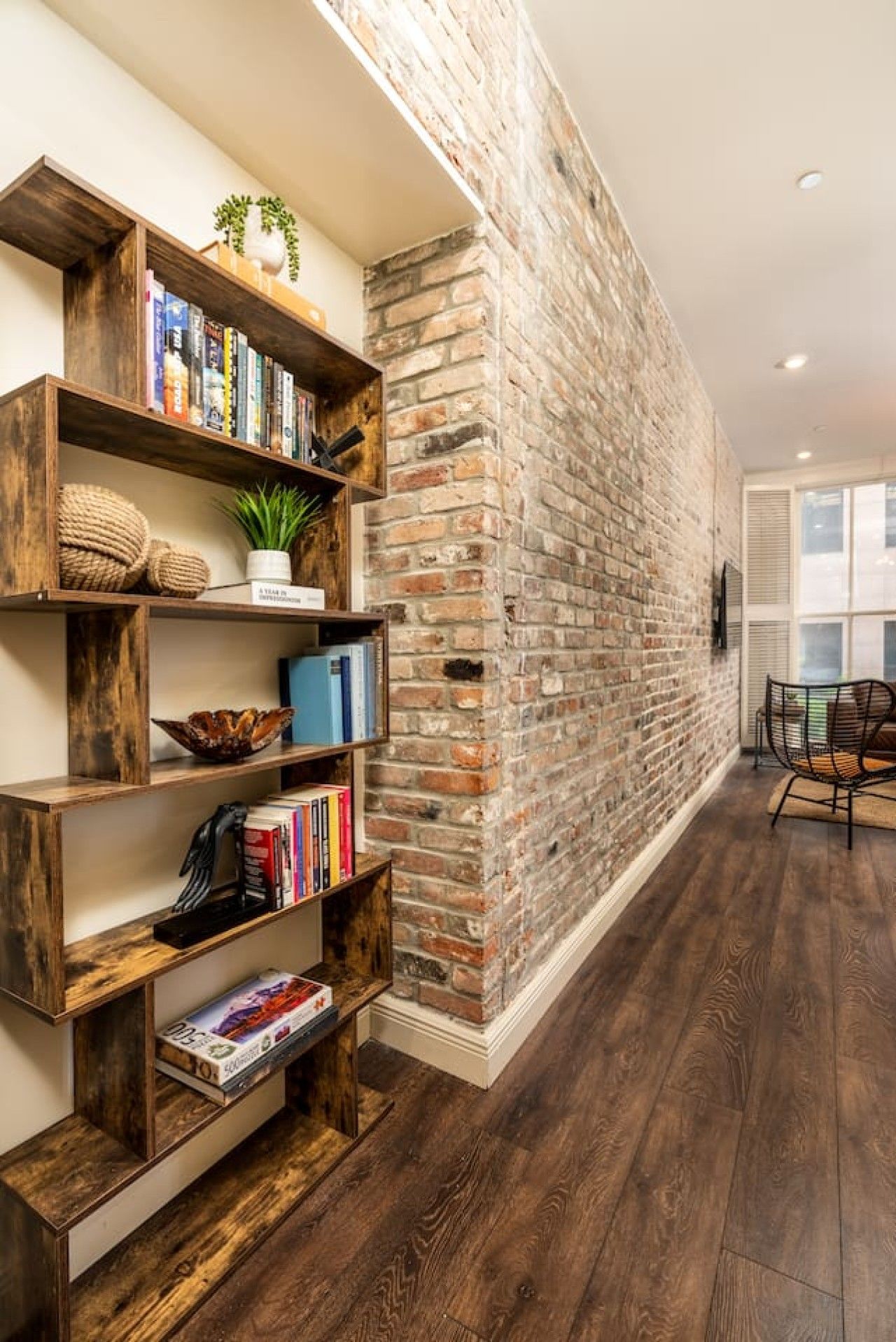 A room with a brick wall, wooden bookshelves, and a dining area with a chair.