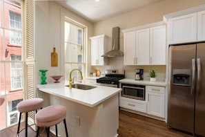 A kitchen with white cabinets, a stainless steel refrigerator, a gas stove, and a sink with a gold faucet. - Group-Friendly NOLA Stay | Steps to French Quarter (New Orleans)