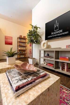 A modern living room with a flat-screen TV, a bookshelf, a potted plant, and a magazine on a coffee table. - Group-Friendly NOLA Stay | Steps to French Quarter (New Orleans)