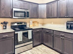 A kitchen with dark wood cabinets, a stainless steel stove, a microwave, and a granite countertop. - Pontiac Lubbock - 3-Bedroom Home in Lubbock, Texas (Lubbock)