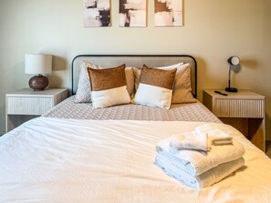A neatly made bed with a white comforter and pillows, a lamp on a bedside table, and a folded towel on the bed. - Pontiac Lubbock - 3-Bedroom Home in Lubbock, Texas (Lubbock)