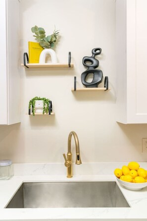 A kitchen with a white countertop, a gold faucet, and a bowl of lemons. - Prime NOLA Stay | 2BD Near Bourbon + Canal (New Orleans)