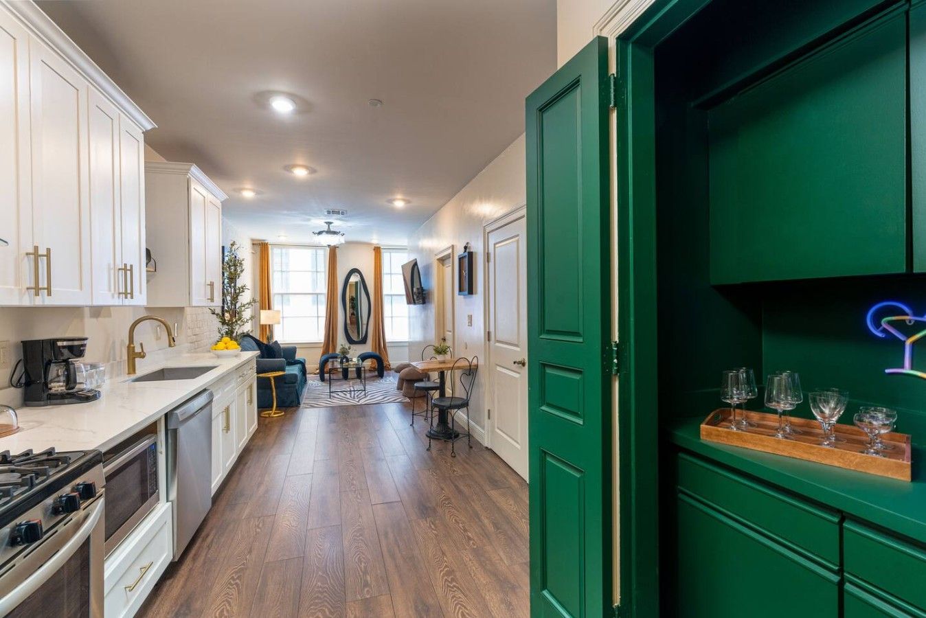 Una cocina moderna con armarios blancos, suelo de madera y una puerta verde.