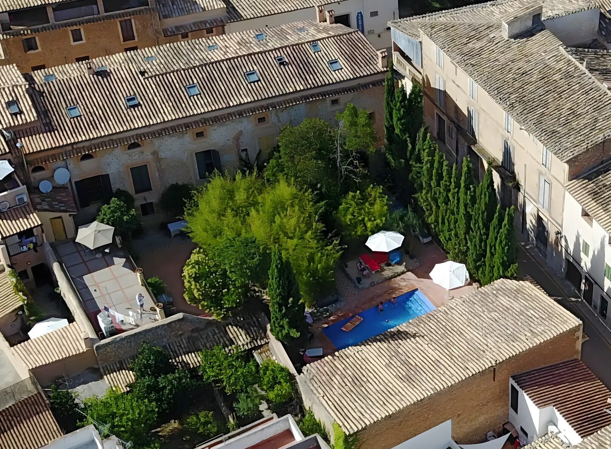 Une vue aérienne d’une cour avec une piscine, entourée de bâtiments aux toits de tuiles et de verdure.