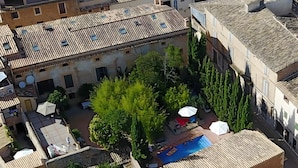 En vy från ovan över en innergård med en swimmingpool, omgiven av byggnader med tak av terrakottafärgat tegel och grönska.