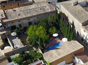 Vista aérea de un patio con piscina, rodeado de edificios con tejados de teja y vegetación.