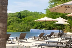 A poolside area with lounge chairs and umbrellas, surrounded by lush greenery. - 3 BR · 2 Pools · Jungle Club · Beach Club (La Cruz de Huanacaxtle)