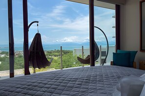 A bedroom with a large bed, a view of the sea, and a hanging chair. - 3 BR · 2 Pools · Jungle Club · Beach Club (La Cruz de Huanacaxtle)