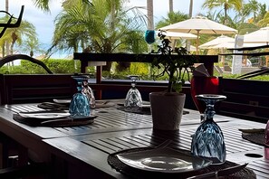 A wooden table set for dining with a view of palm trees and a clear sky. - 3 BR · 2 Pools · Jungle Club · Beach Club (La Cruz de Huanacaxtle)