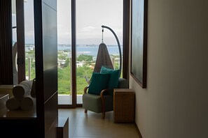 Une chambre moderne avec une grande fenêtre, un fauteuil avec un coussin, une petite table et un téléviseur.