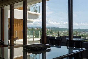 A modern interior with a glass partition, a dining area with a table, and a view of a cityscape and mountains. - 3 BR · 2 Pools · Jungle Club · Beach Club (La Cruz de Huanacaxtle)