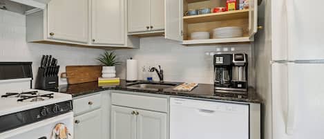 Una cocina con armarios blancos, estufa, lavavajillas y cafetera.
