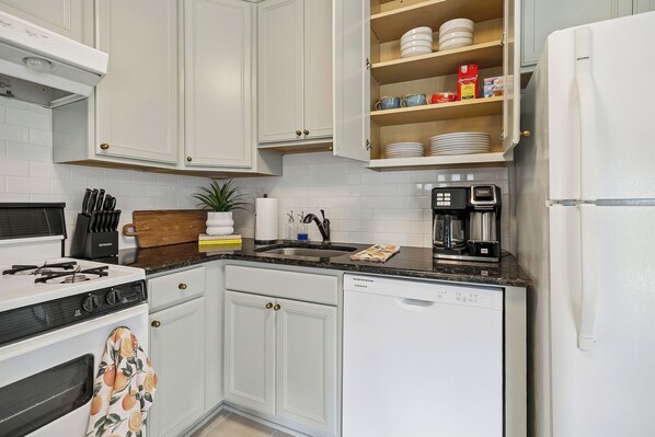 A kitchen with white cabinets, a stove, a dishwasher, and a coffee maker.