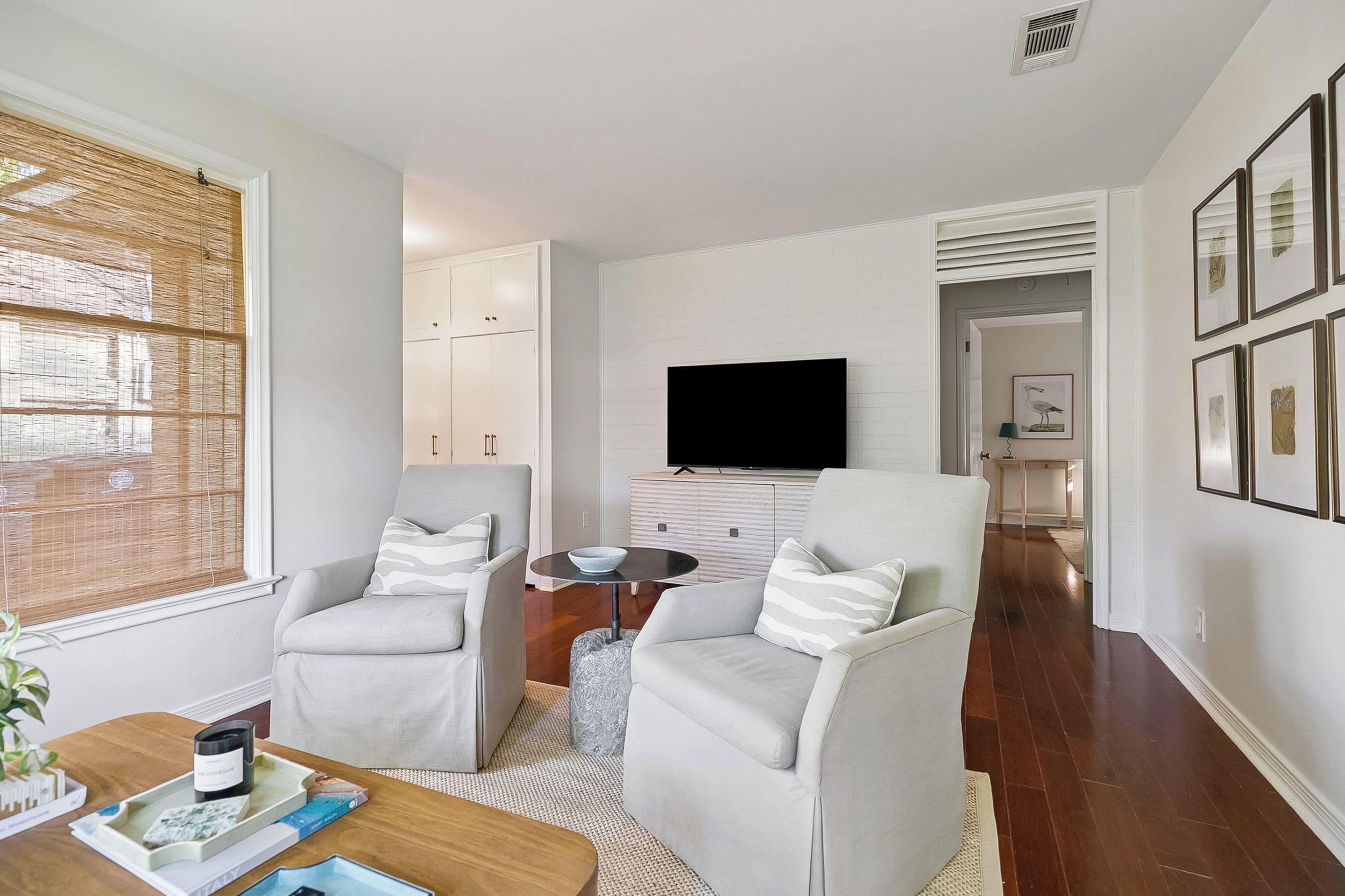 A modern living room with two armchairs, a coffee table, a flat-screen TV mounted on the wall, and a small side table.