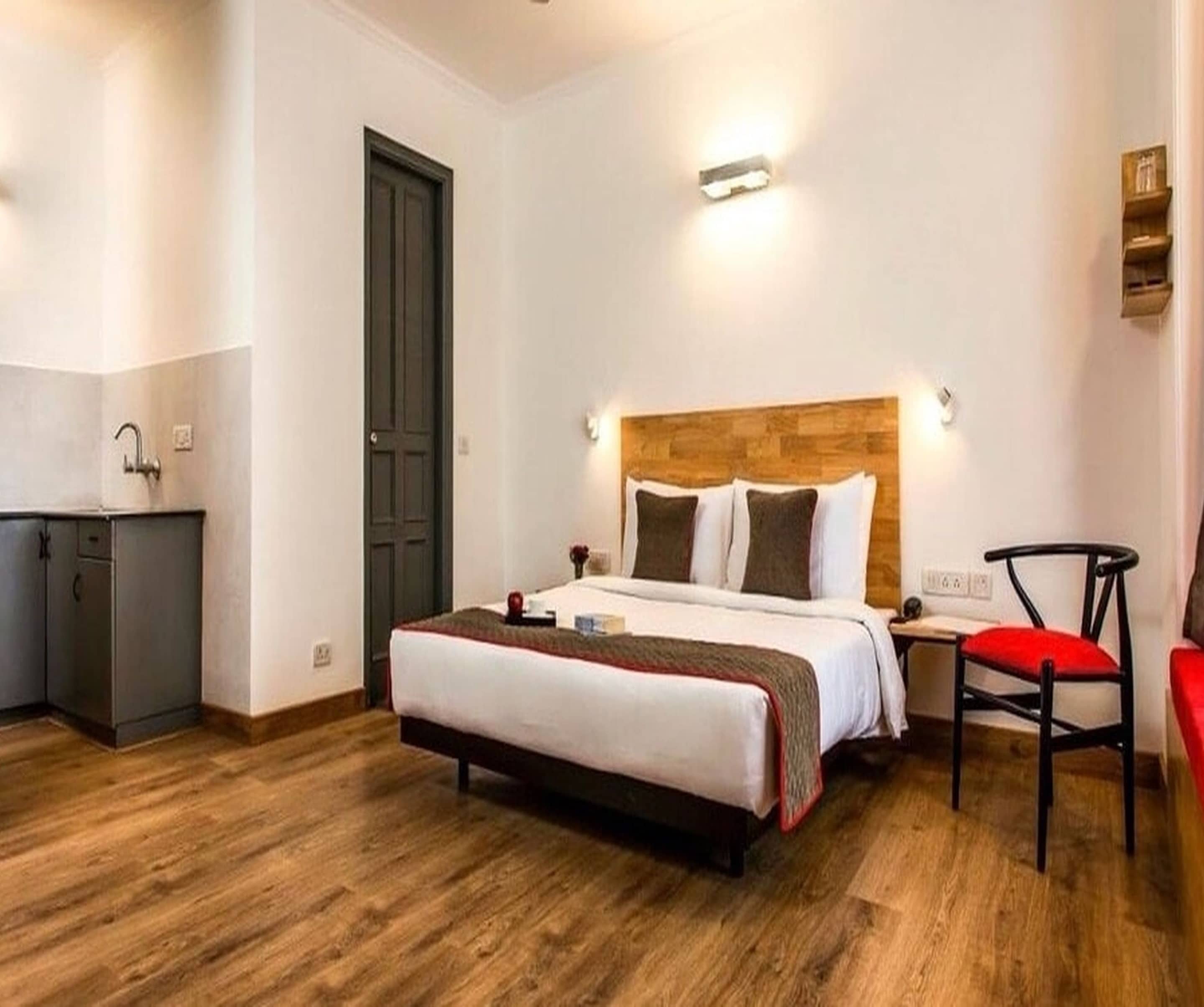 A hotel room with a bed, bedside table, chair, and a small desk with a chair.