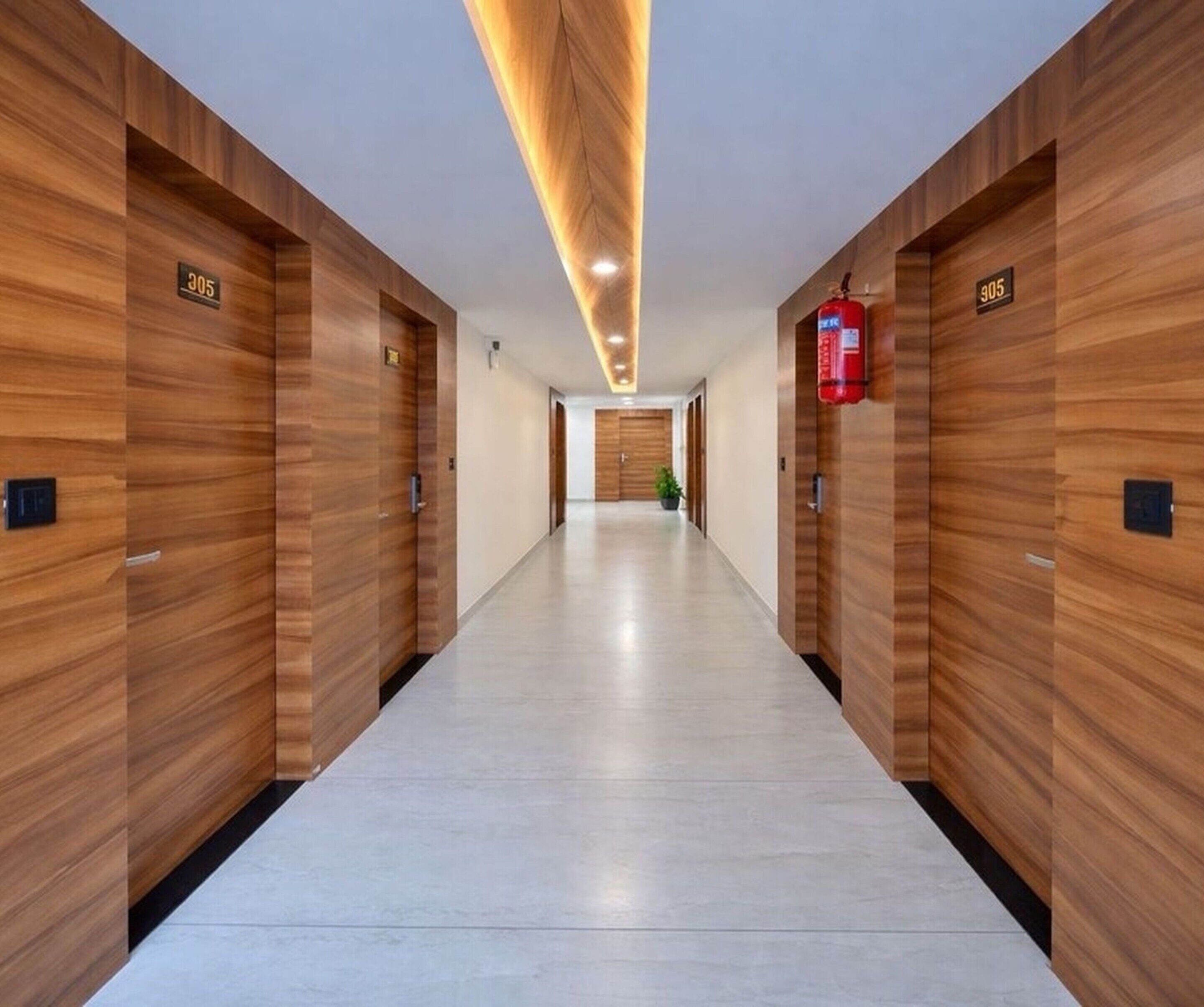 Un couloir aux murs recouverts de lambris en bois, avec des portes numérotées, un extincteur et un plafond doté d’un éclairage encastré.