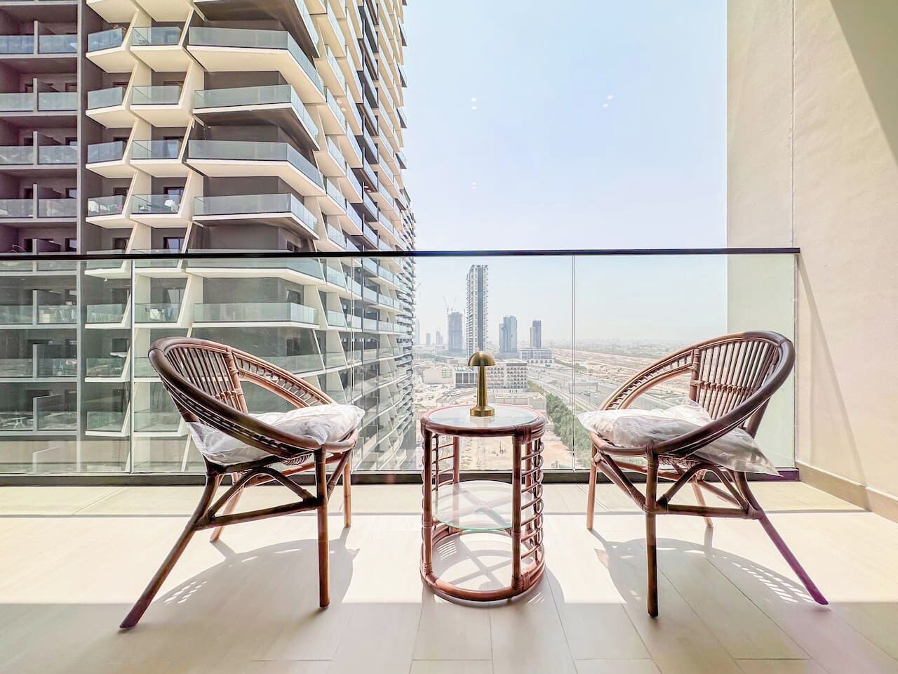 A balcony with two wicker chairs and a small round table, overlooking a cityscape.
