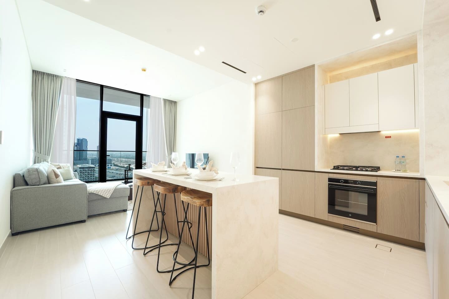 A modern kitchen with a central island, bar stools, and a view of the city through large windows.
