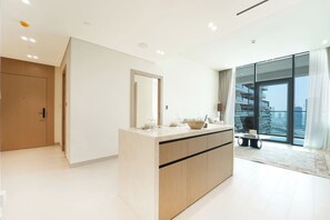 Ein modernes Interieur mit einer zentralen Kücheninsel, einem großen Spiegel und Blick auf eine Stadtlandschaft durch raumhohe Fenster.