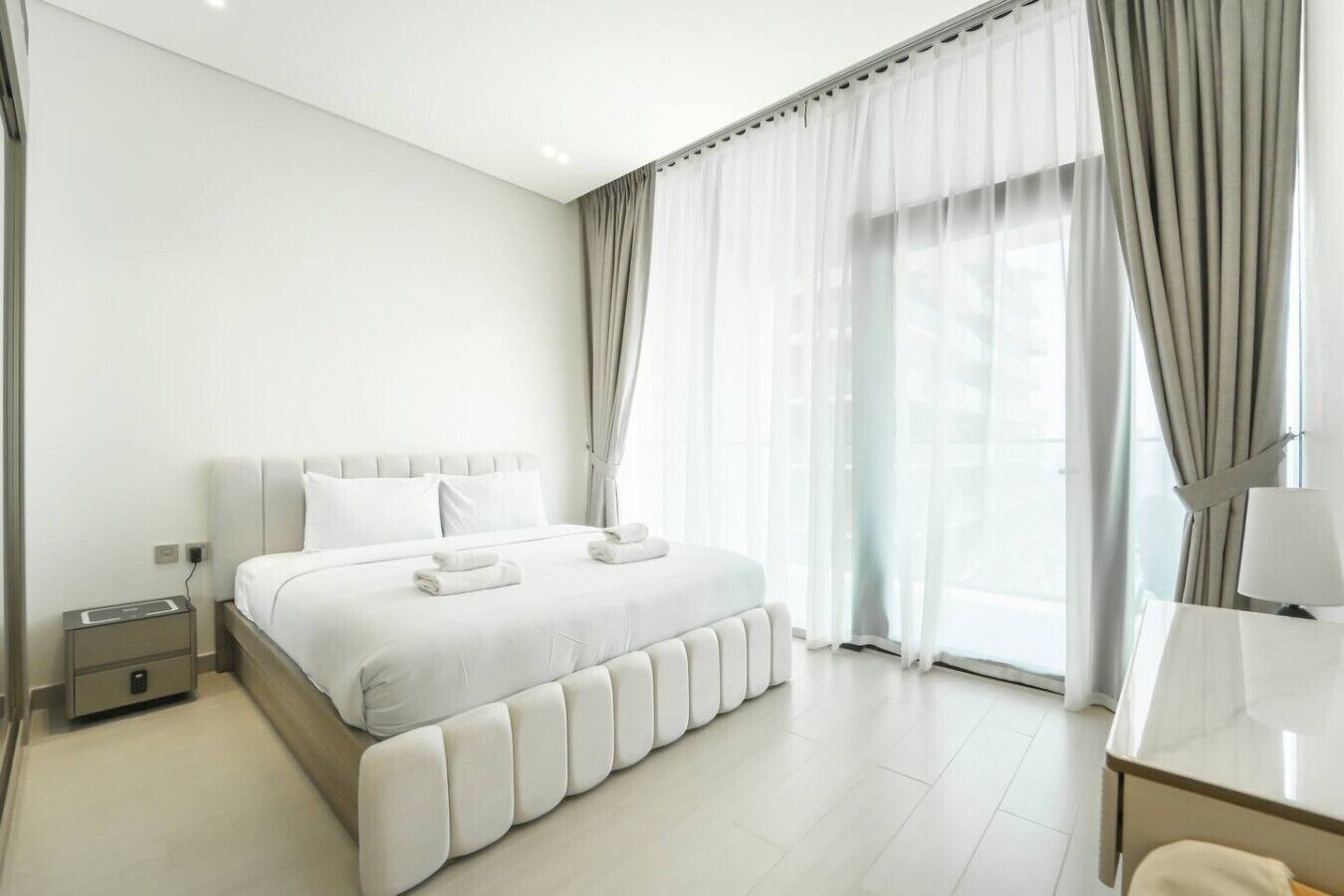 Quarto de hotel moderno com uma cama grande, uma mesa de cabeceira e uma escrivaninha com abajur.