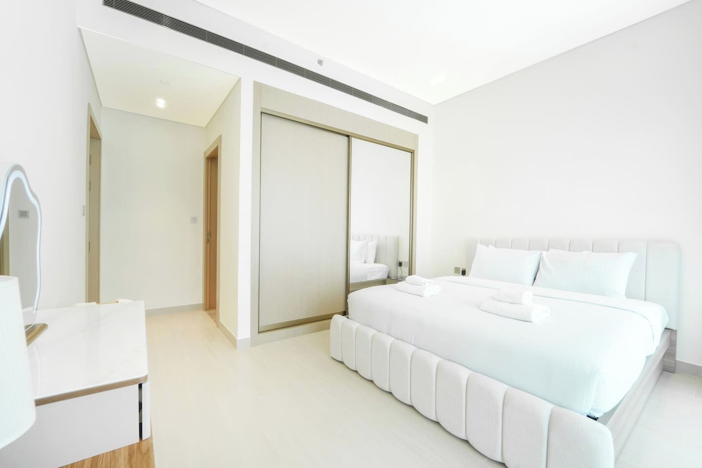Habitación de hotel moderna con una cama grande, una mesita de noche, un armario y un baño visible a través de una puerta abierta.