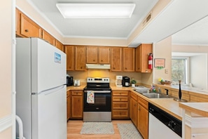 A compact kitchen with wooden cabinets, a refrigerator, a stove, and a dishwasher. - Tilghman 138- 3BR Ocean Drive Condo with Pool (North Myrtle Beach)