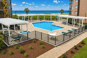 A pool area with a view of the ocean, surrounded by lounge chairs and covered seating. - Tilghman 138- 3BR Ocean Drive Condo with Pool (North Myrtle Beach)
