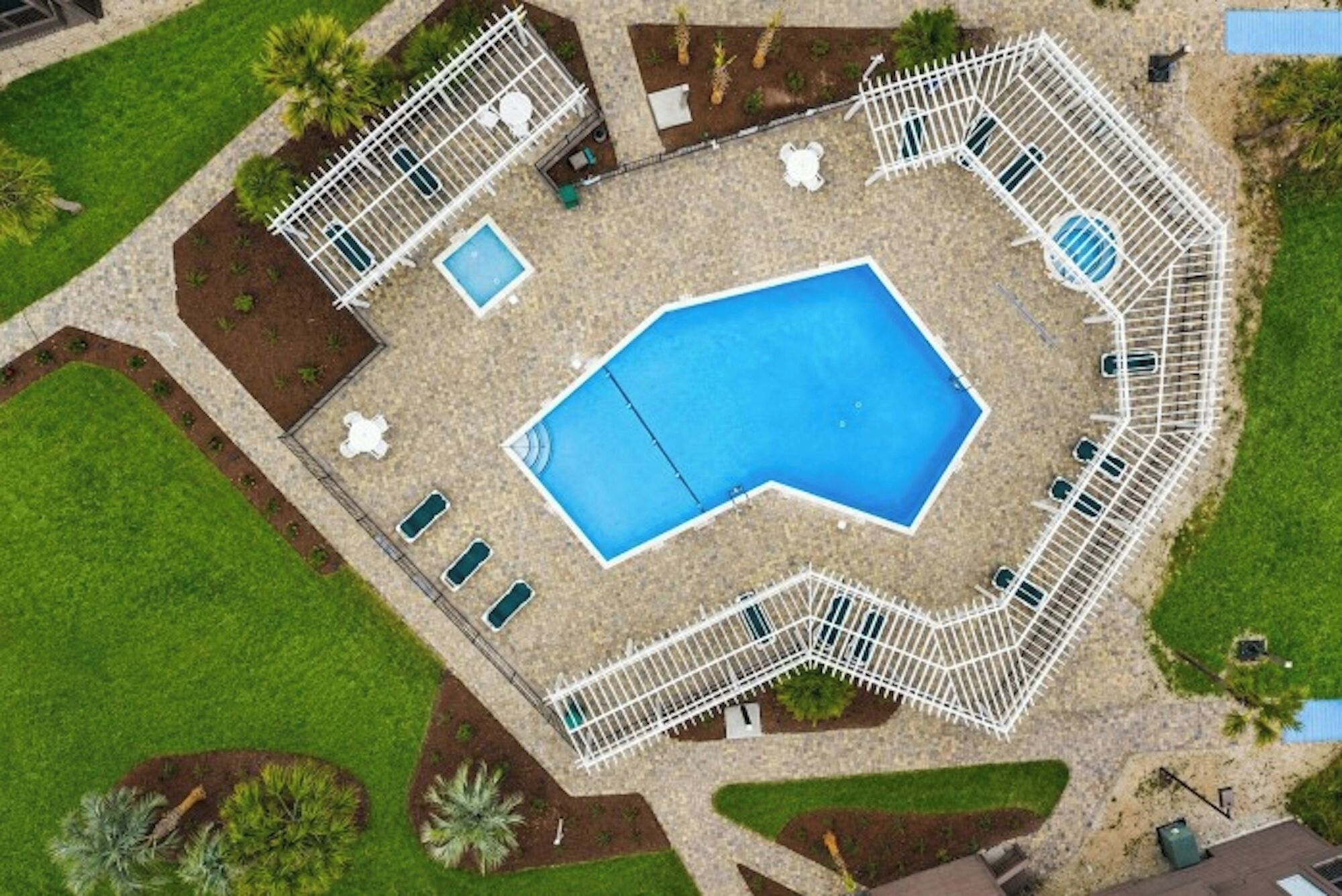 An aerial view of a swimming pool surrounded by a white fence, with multiple lounge chairs and a small deck area.