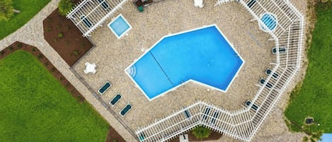 An aerial view of a swimming pool surrounded by a white fence, with multiple lounge chairs and a small deck area.