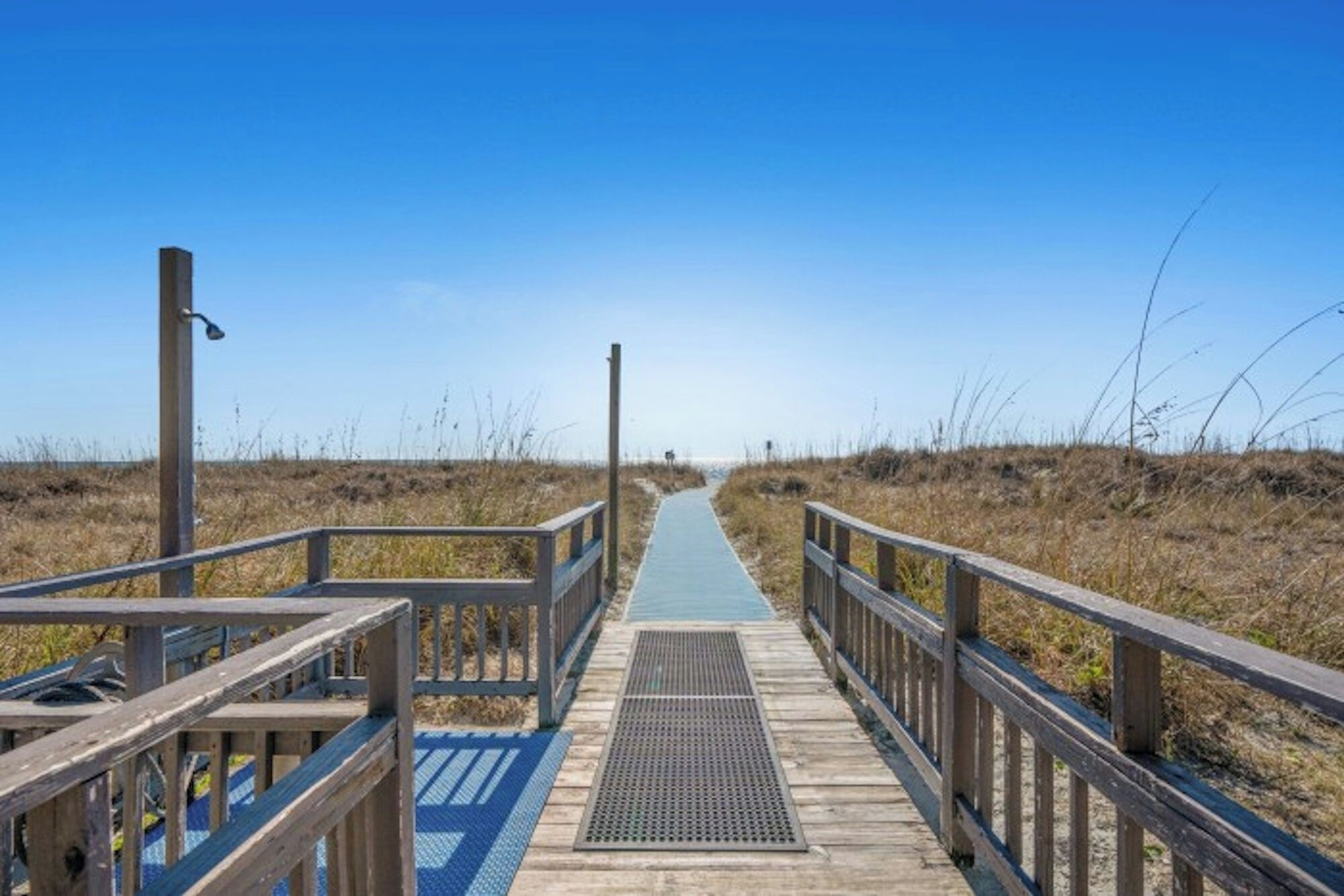 A wooden boardwalk leading to a beach with a clear sky.