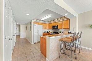 A kitchen with wooden cabinets, a refrigerator, a microwave, and a granite countertop. - Oceanfront Crescent Shores 1204- 2 BR- Hot Tub (North Myrtle Beach)