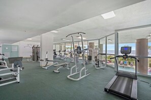 A gym with various exercise equipment, a treadmill, and large windows offering a view. - Oceanfront 2BR Crescent Keyes 1103- I/O Pools (North Myrtle Beach)