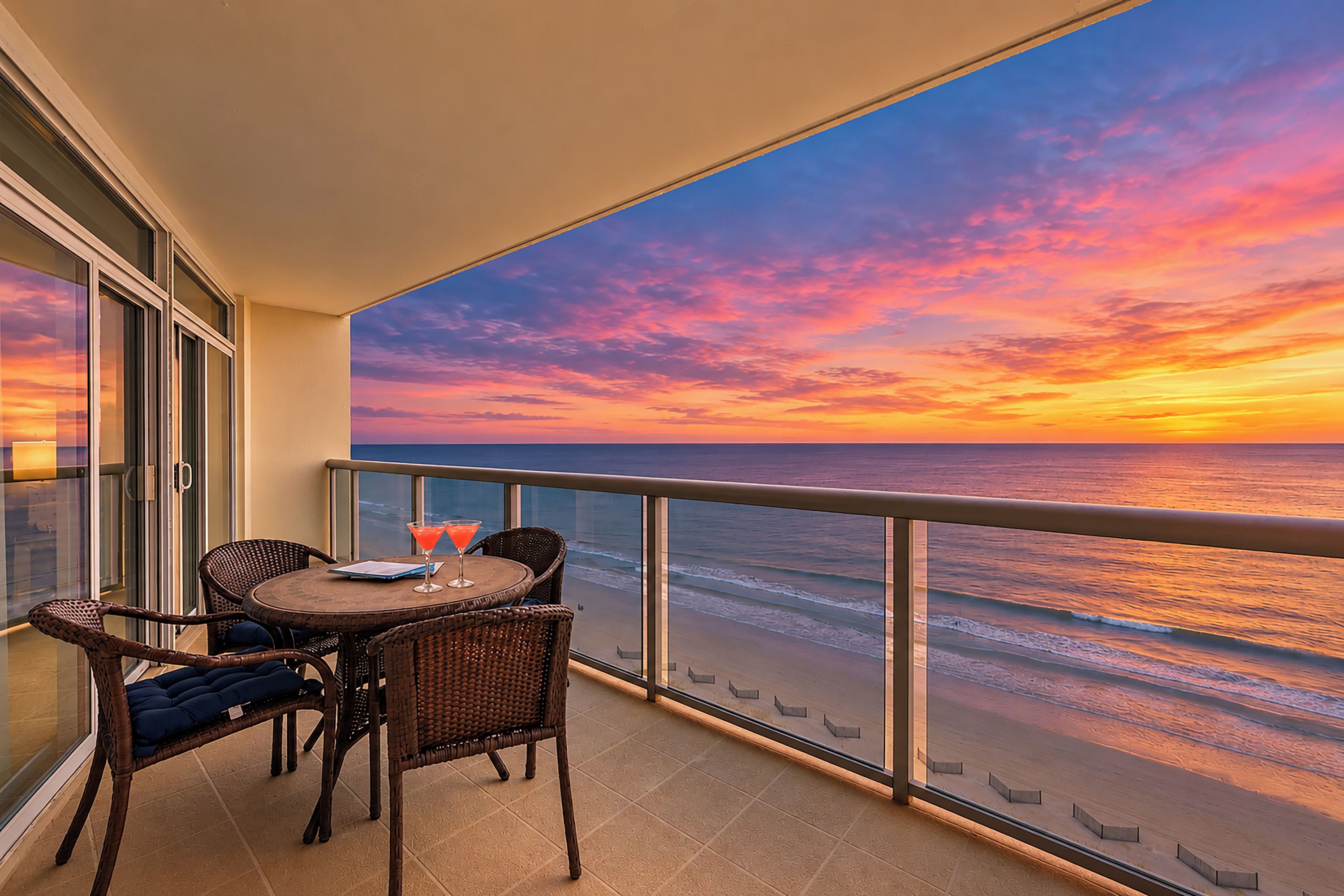 Ein Balkon mit Blick auf das Meer bei Sonnenuntergang, ausgestattet mit Tisch und Stühlen.