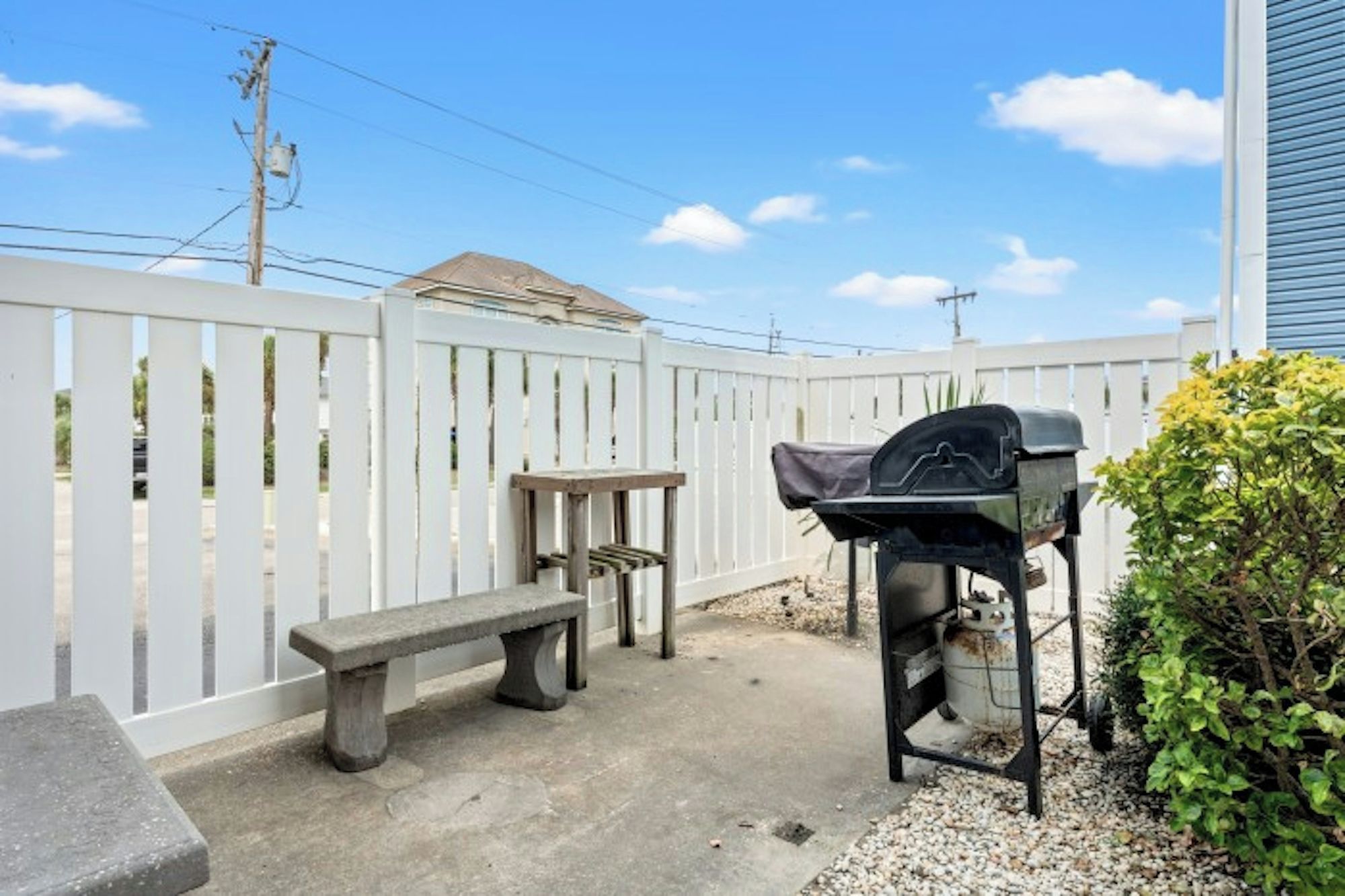 A backyard with a barbecue grill, a bench, and a white fence.