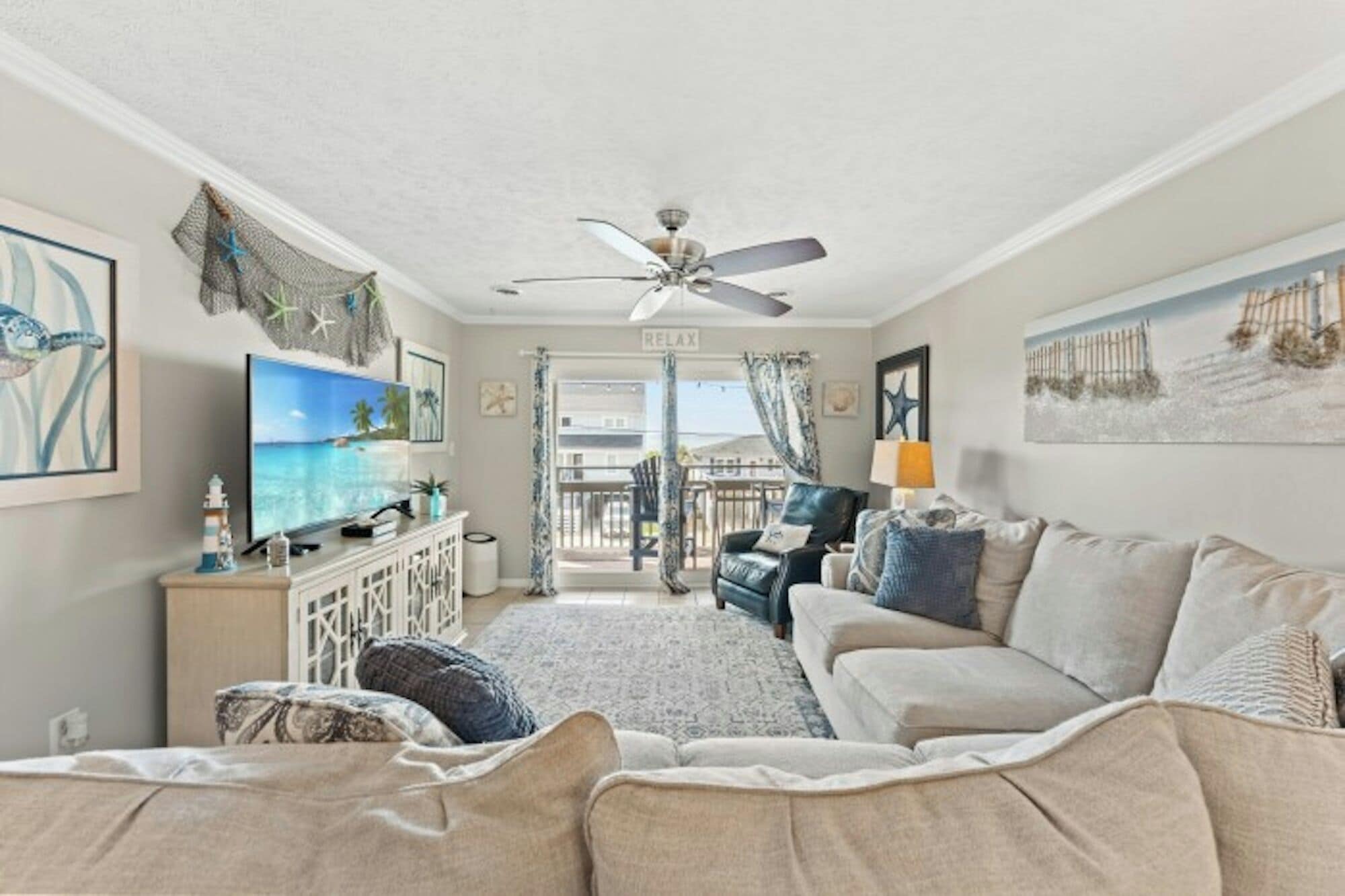 Una sala de estar con ventilador de techo, televisor, sofá y vista al exterior.