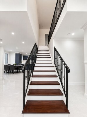 Uma escadaria com degraus brancos e guarda-corpo preto, levando a um andar superior.