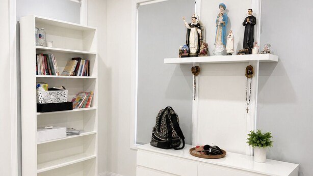 A modern living room with a white bookshelf, a console table with religious statues, a brown sofa, and a small round table with a book. - Luxury Family Retreat in Chipping Norton (Chipping Norton)