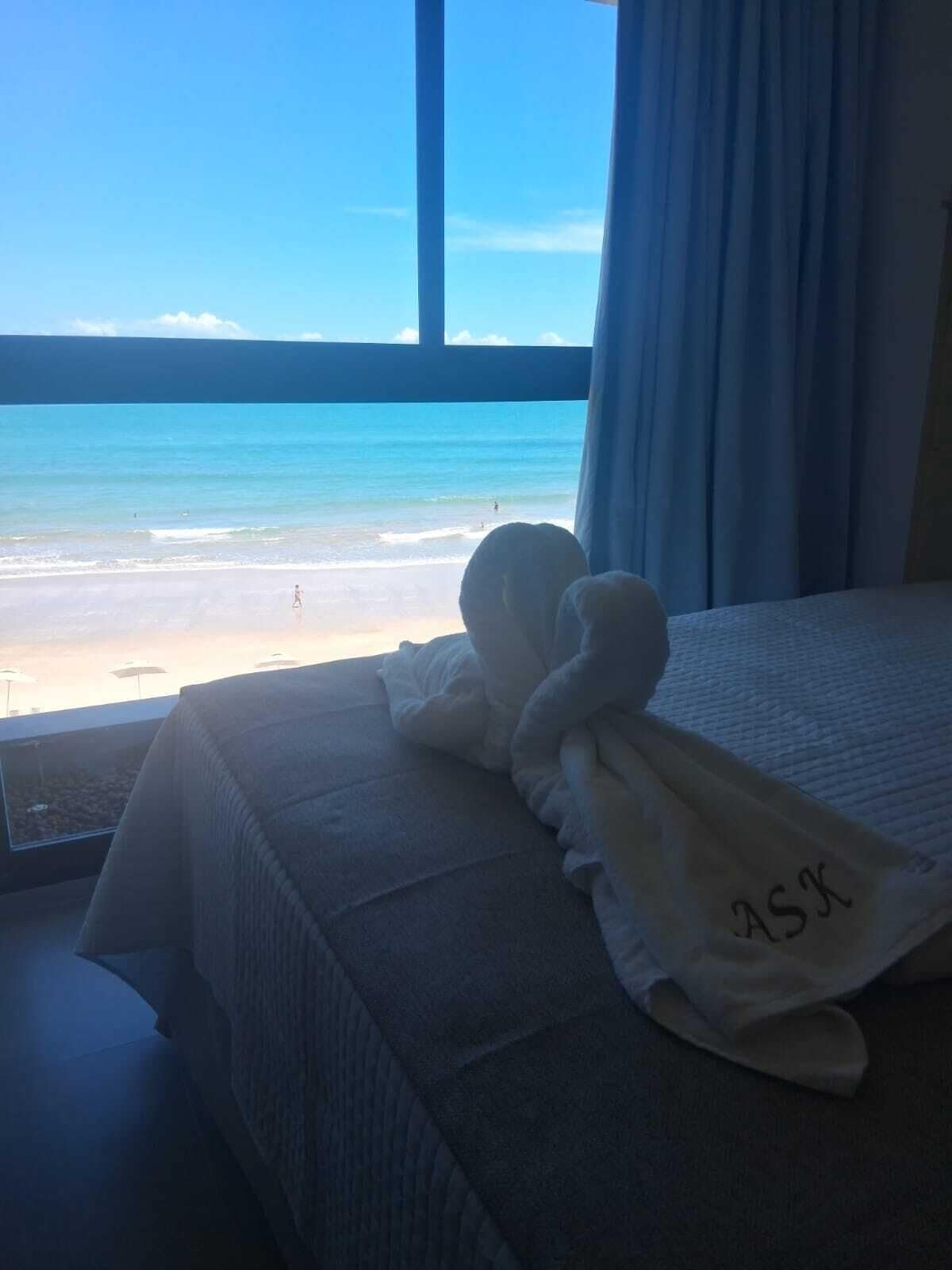 A bed with a view of the beach and ocean through a window.