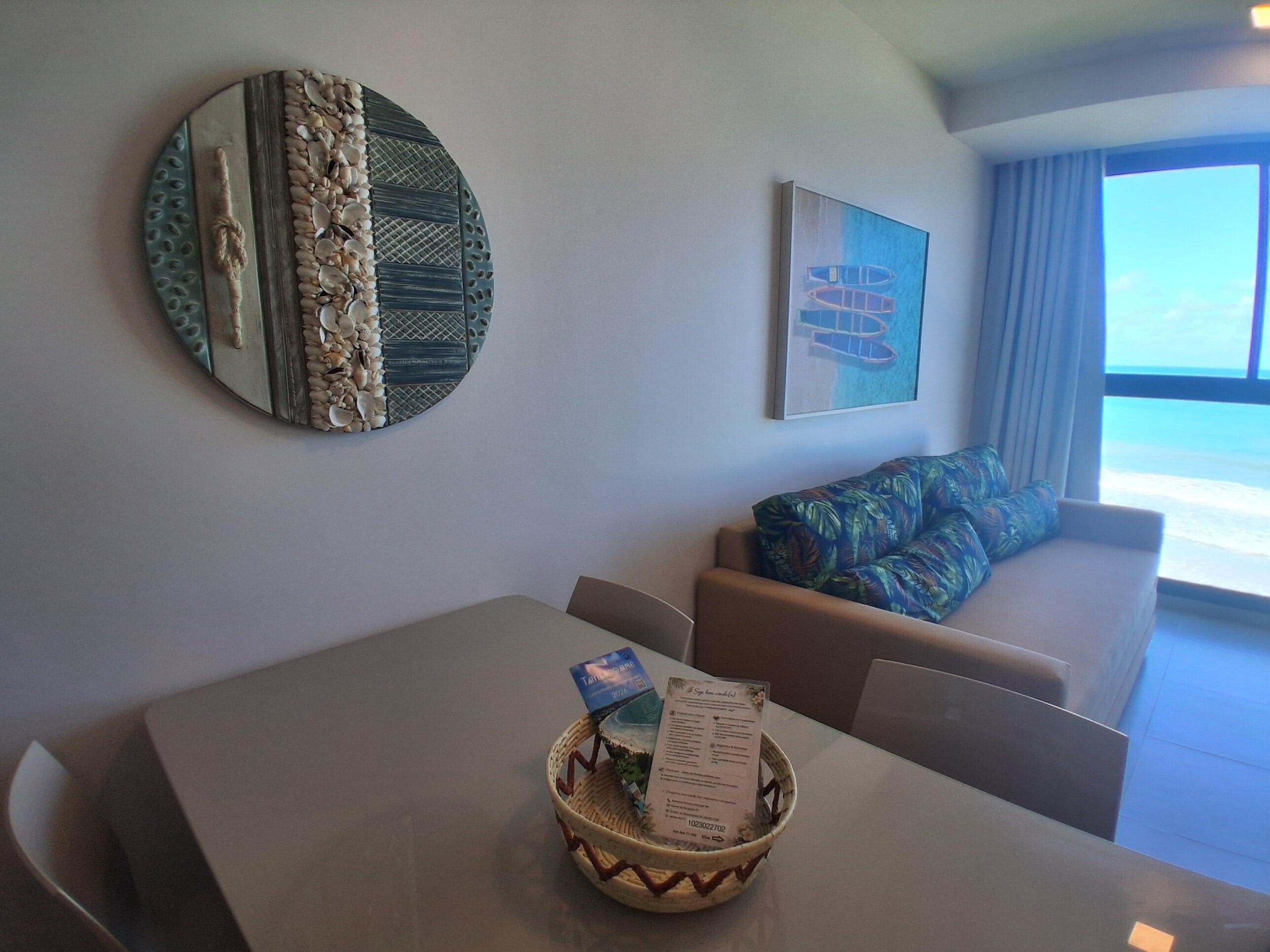 Een kamer met een eettafel, een bank met opvallende kussens, een decoratief object aan de muur en een raam met uitzicht.