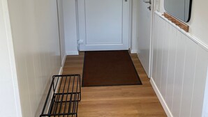 Un couloir avec une porte blanche, un paillasson marron et un porte-manteau en métal.