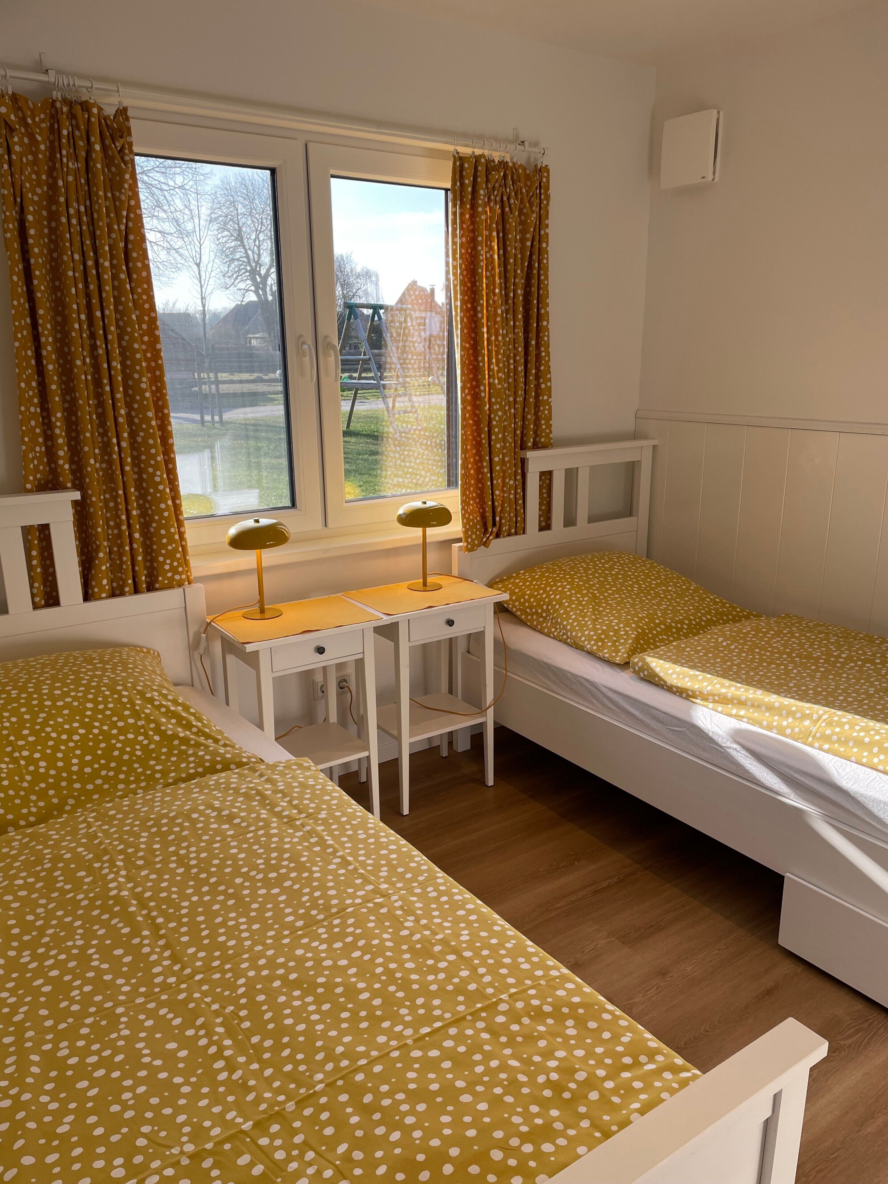 Ein Zimmer mit zwei Betten, einem Schreibtisch und einem Fenster mit Vorhängen.
