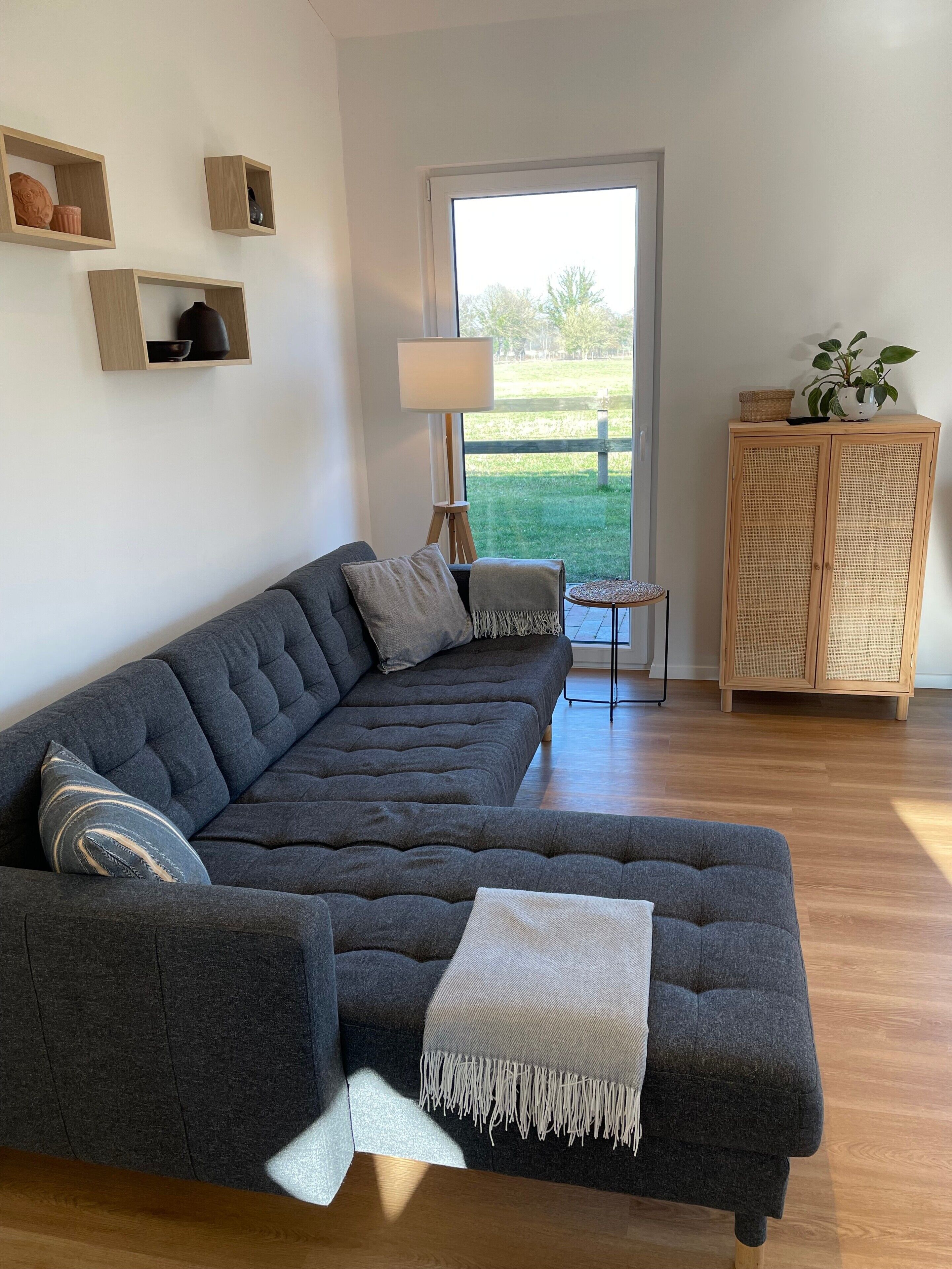 Ein modernes Wohnzimmer mit einem Ecksofa, einem kleinen Beistelltisch, einer Lampe und einem Korbuscheinmöbel.