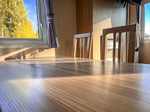 Una mesa de comedor de madera con sillas, una ventana con cortinas y vista a árboles.