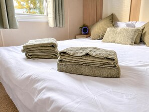 Una cama bien hecha con sábanas blancas y un edredón doblada encima.