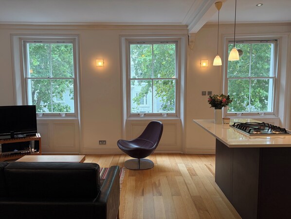 Une cuisine moderne dotée de grandes fenêtres, un coin repas avec un fauteuil en cuir noir et un téléviseur à écran plat posé sur un meuble en bois.