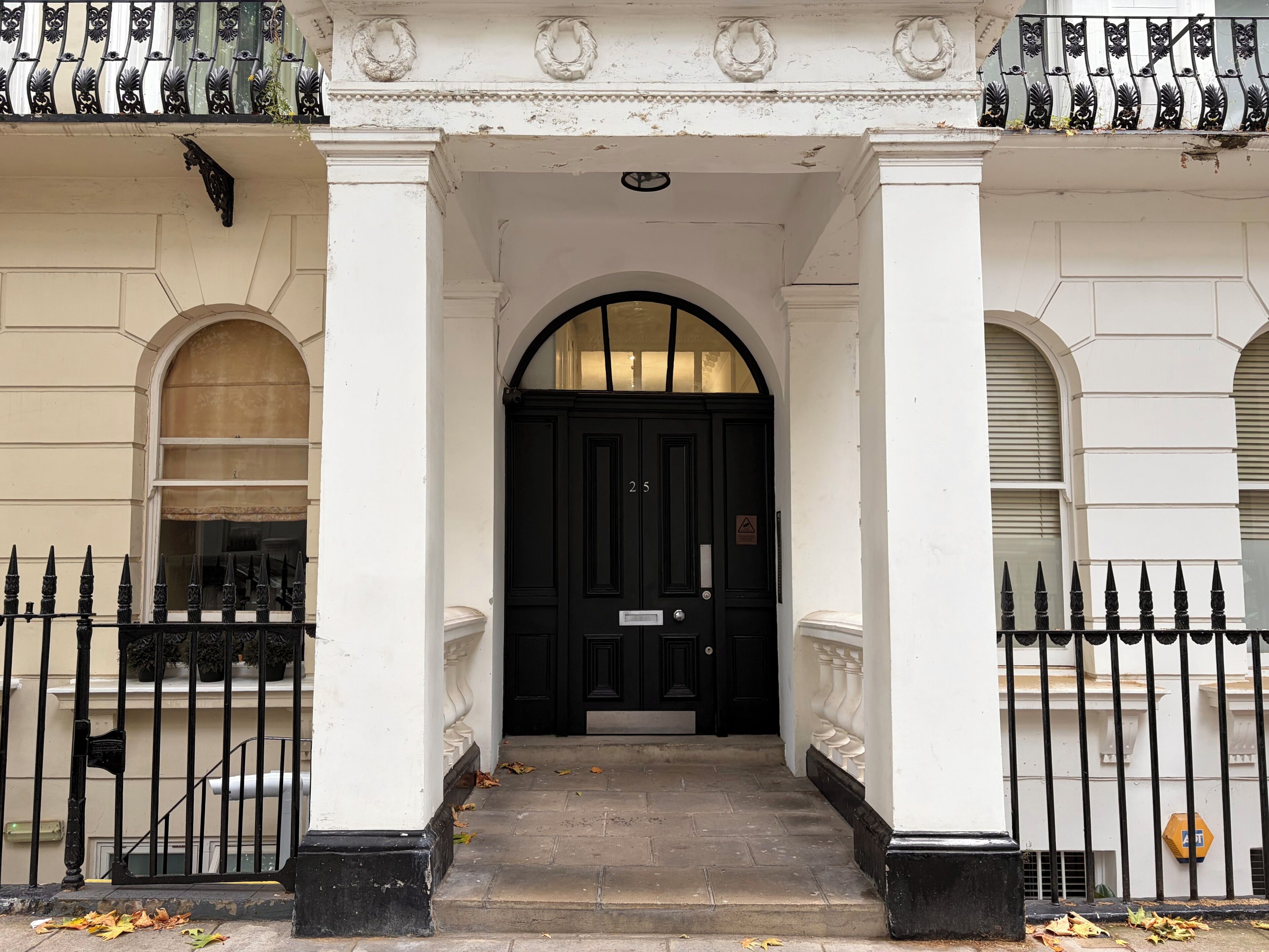 A building entrance with a black door, white columns, and a black metal fence.