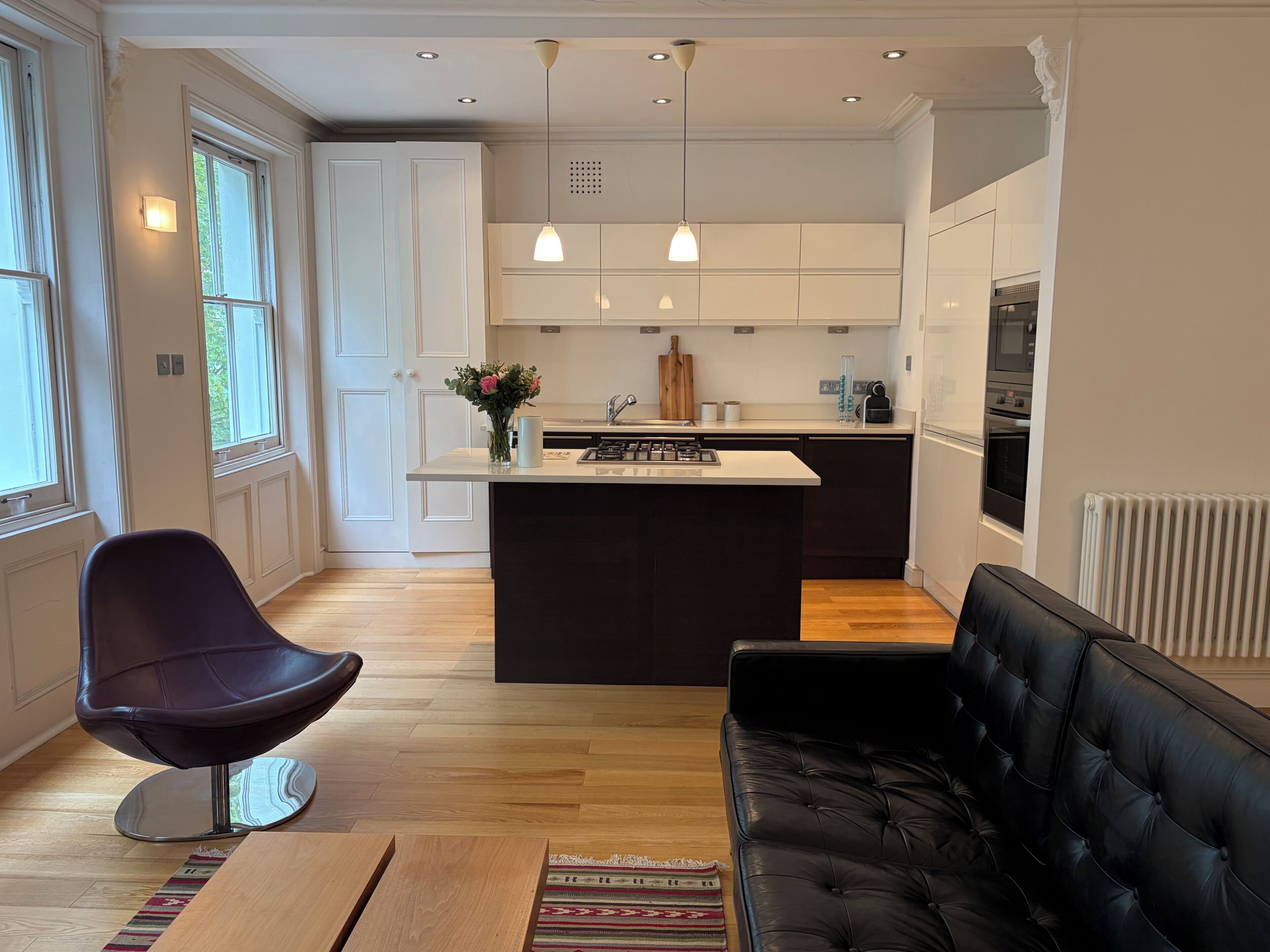 Una cocina moderna con una isla central, iluminación colgante y una zona de comedor con sofá y sillón.