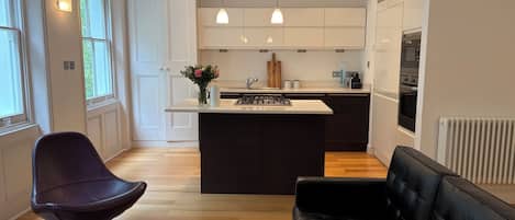 Una cocina moderna con una isla central, iluminación colgante y una zona de comedor con sofá y sillón.